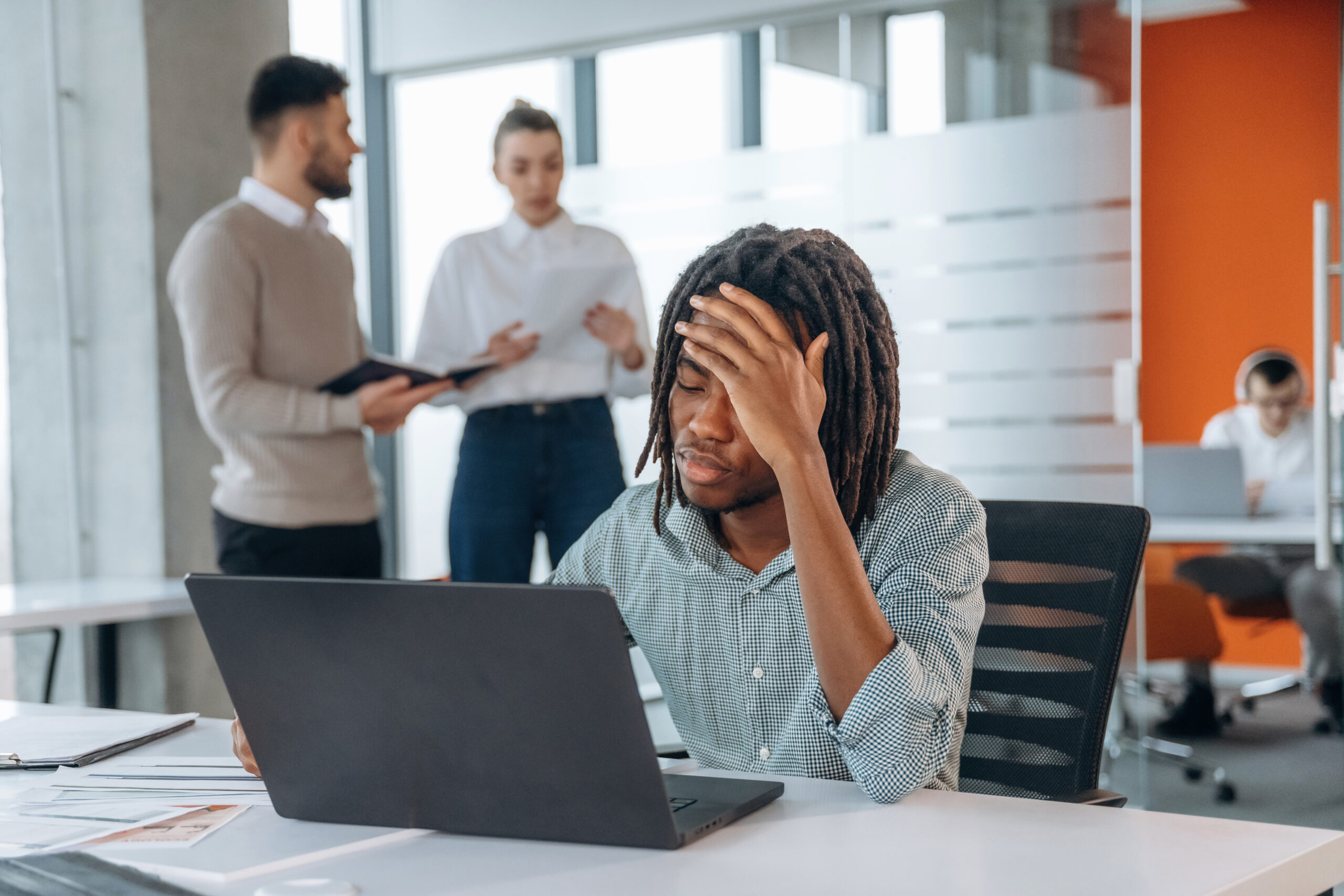 A frustrated young professional sitting in a modern office setting while working on a laptop.